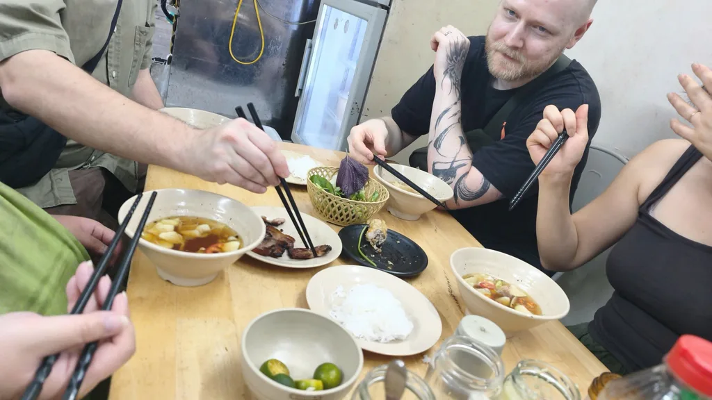 Shared wooden table with rice vermicelli, grilled meat, herbs, broth, and lime — layout consistent with Hanoi bun cha service.