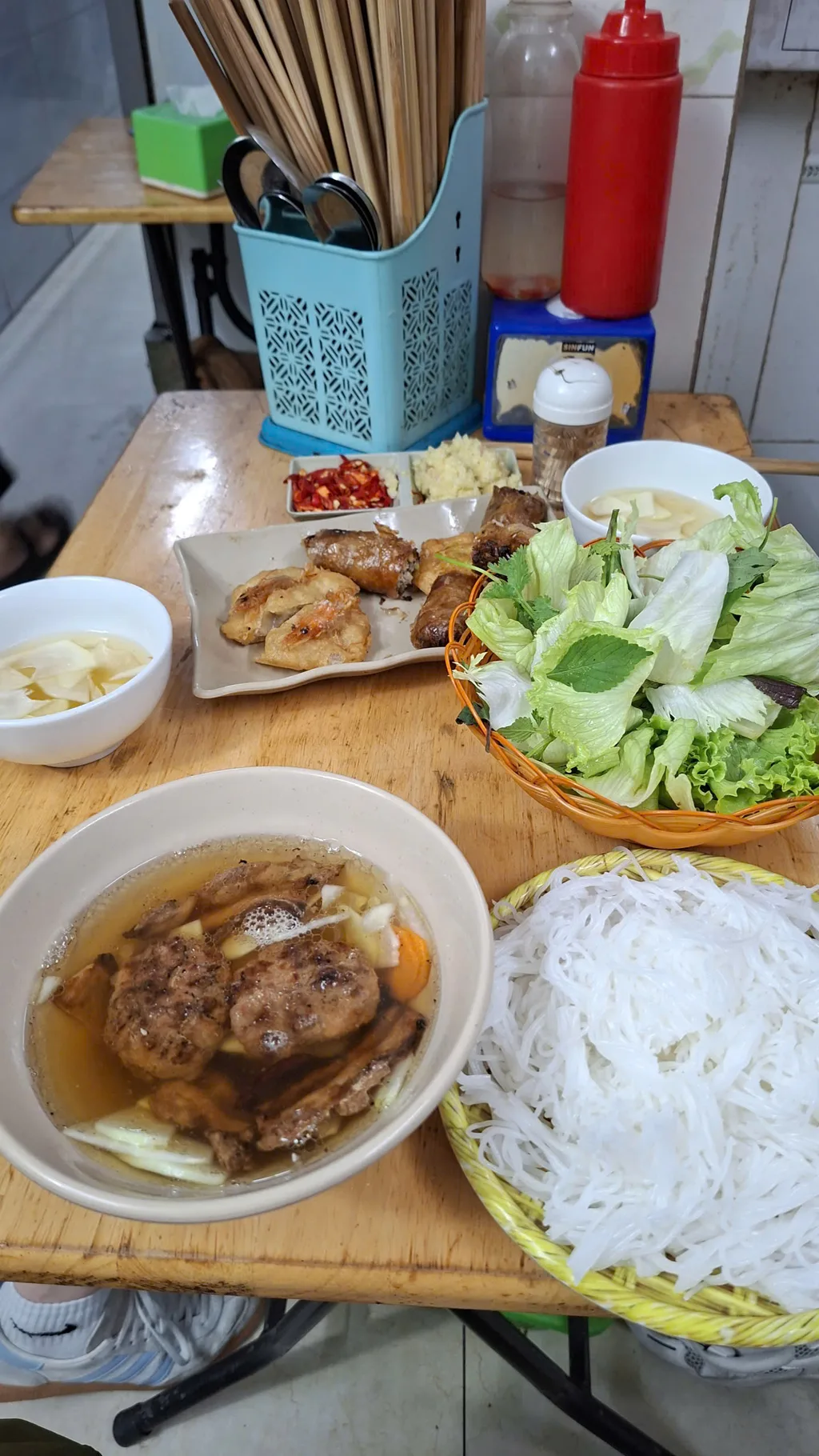 A Hanoi street-food table with noodles, herbs, broth and grilled meat. Dishes vary by stop.