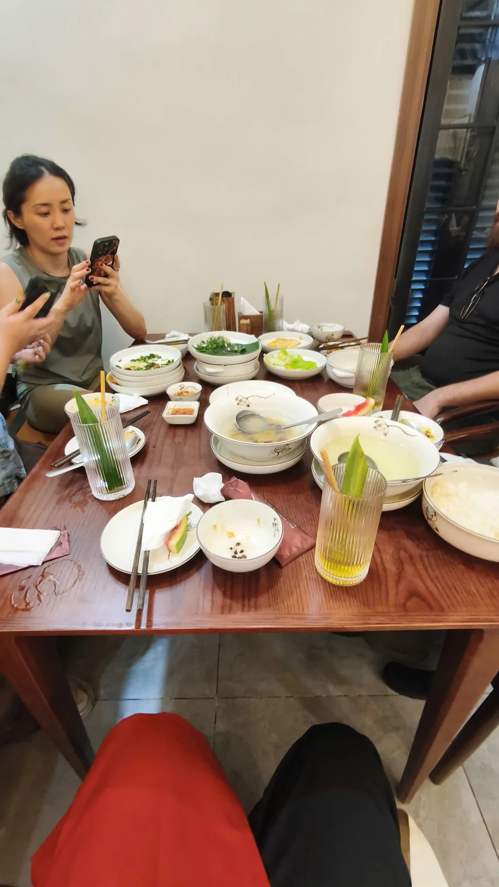 Communal wooden table with shared rice, fresh herbs, and dipping bowls at a Hanoi eatery.