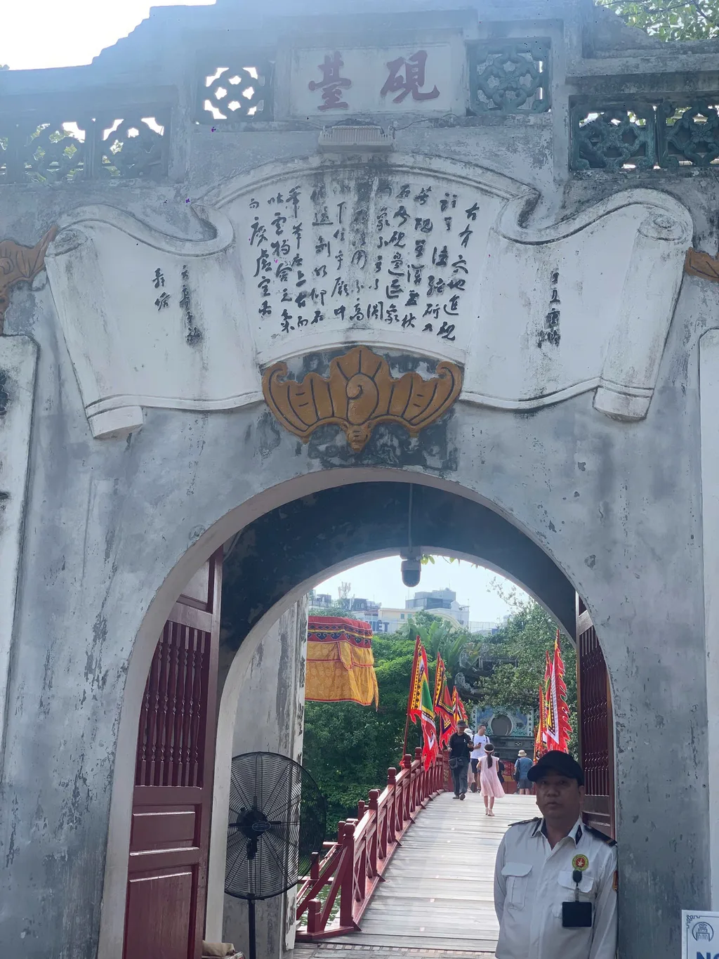Stone gate to Ngoc Son Temple with the red Huc Bridge and lake visible beyond at Hoan Kiem.