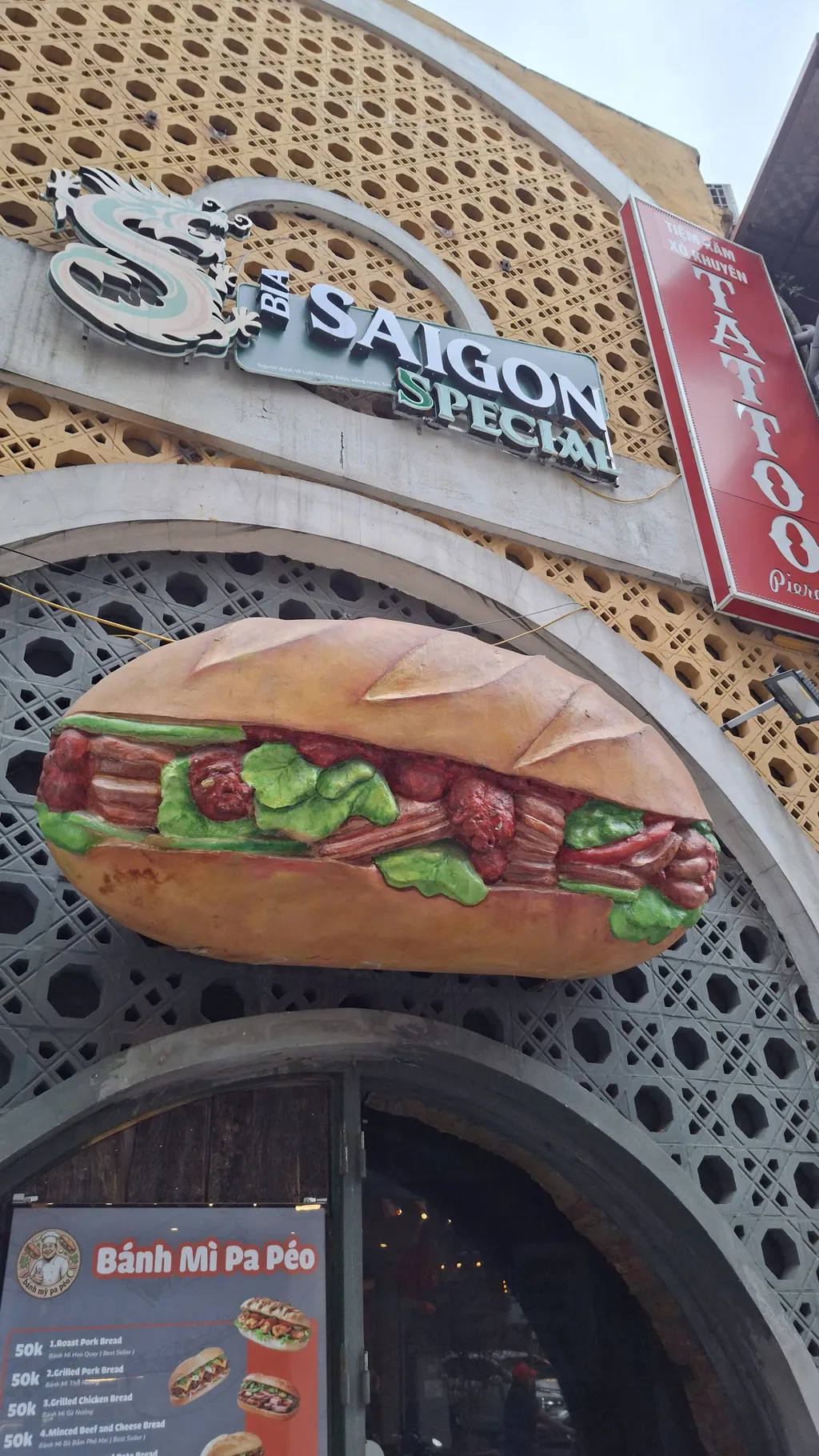 Oversized decorative bánh mì sculpture and painted menu board above a shopfront arch — signage only, not a food-prep or vendor portrait.