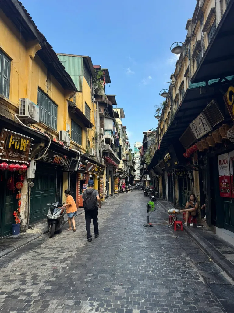 Narrow cobbled Old Quarter street lined with tube-house shopfronts and parked motorbikes.
