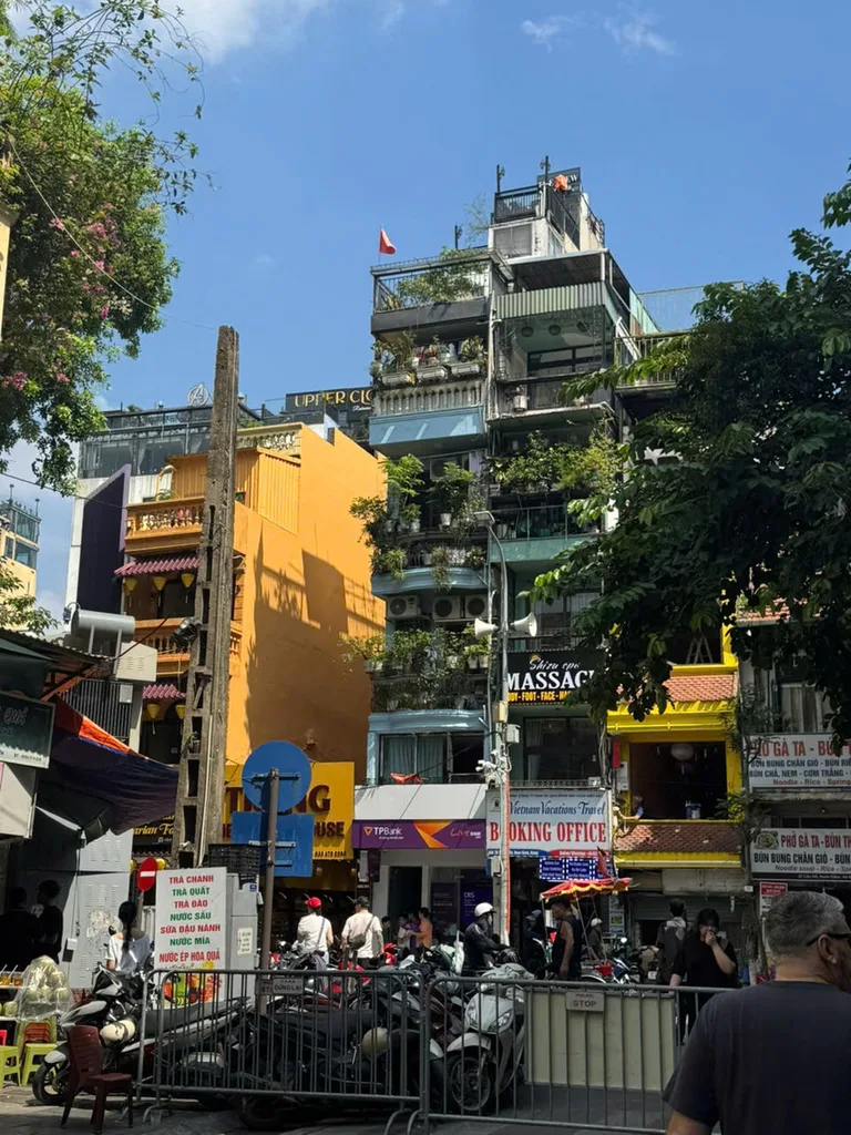 Tall tube-house facades, shop signs, and parked motorbikes on a busy Old Quarter street.