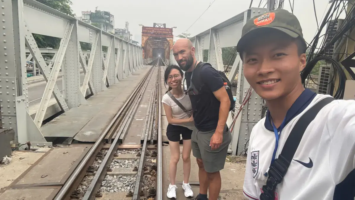Brazilian traveller Matheus and local guide Tommy on the historic Long Bien Bridge railway tracks during a Hanoi walking tour.